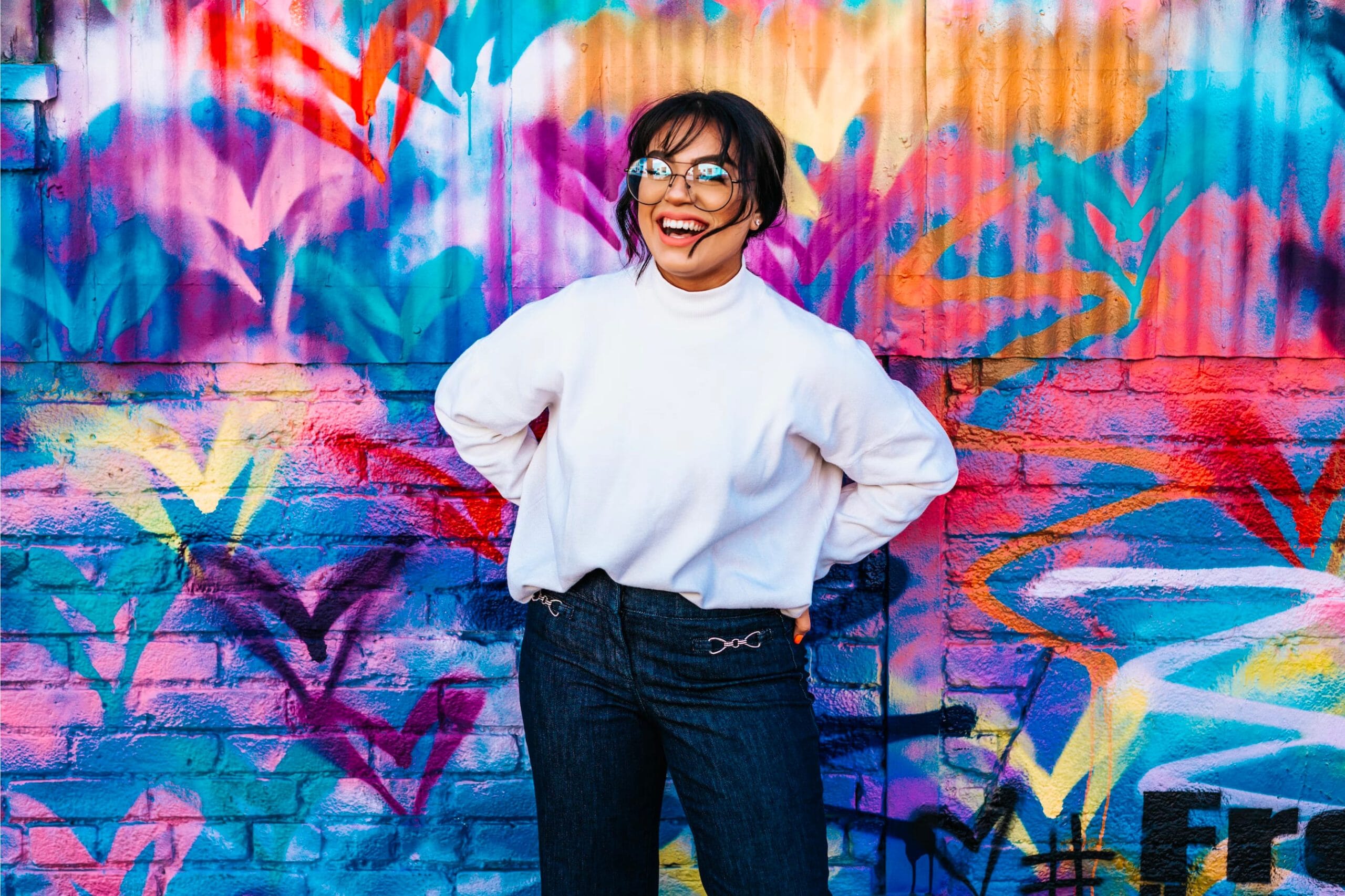 person smiling in front of a colourful graffiti wall
