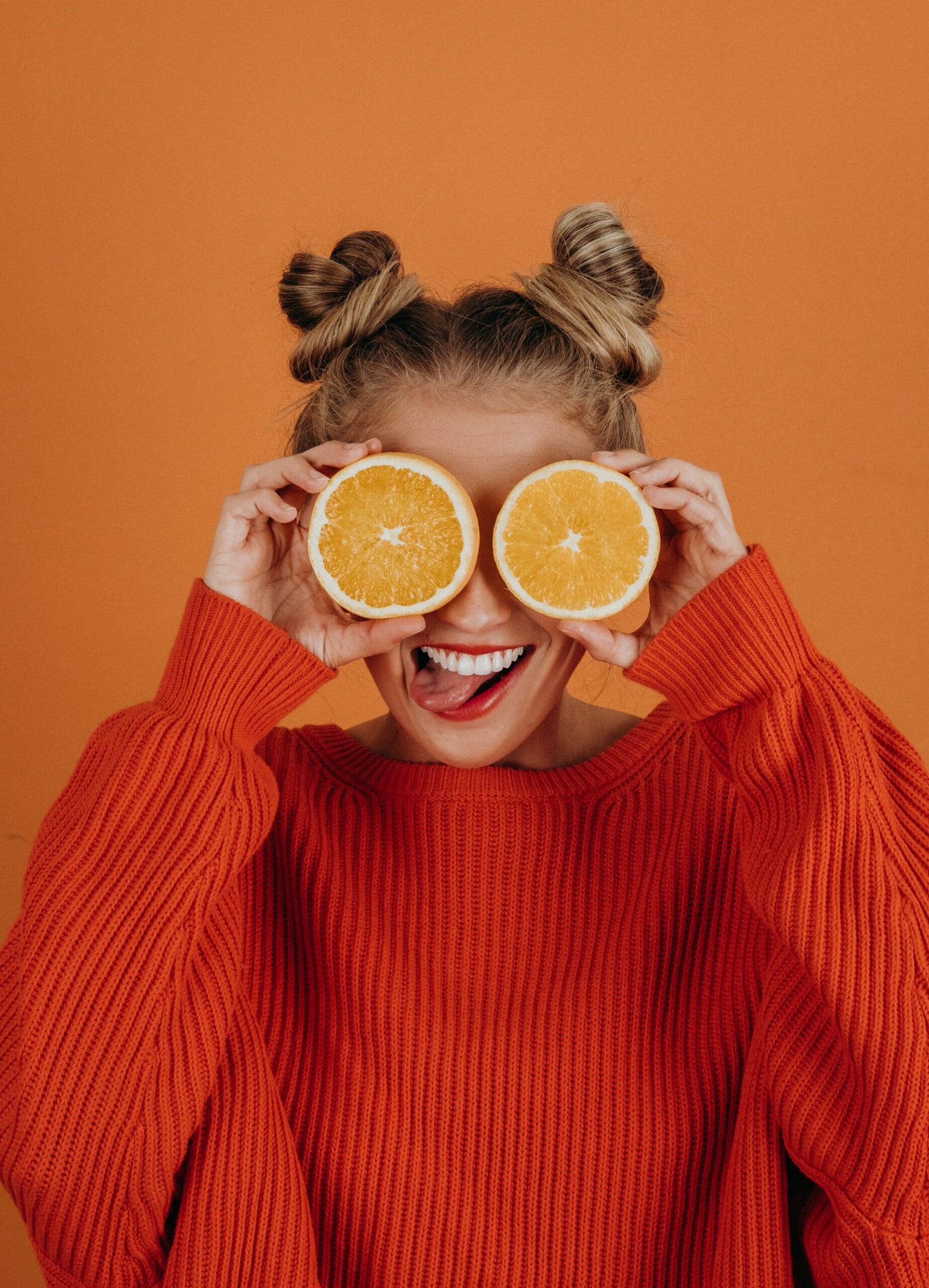 person smiling with oranges over eyes