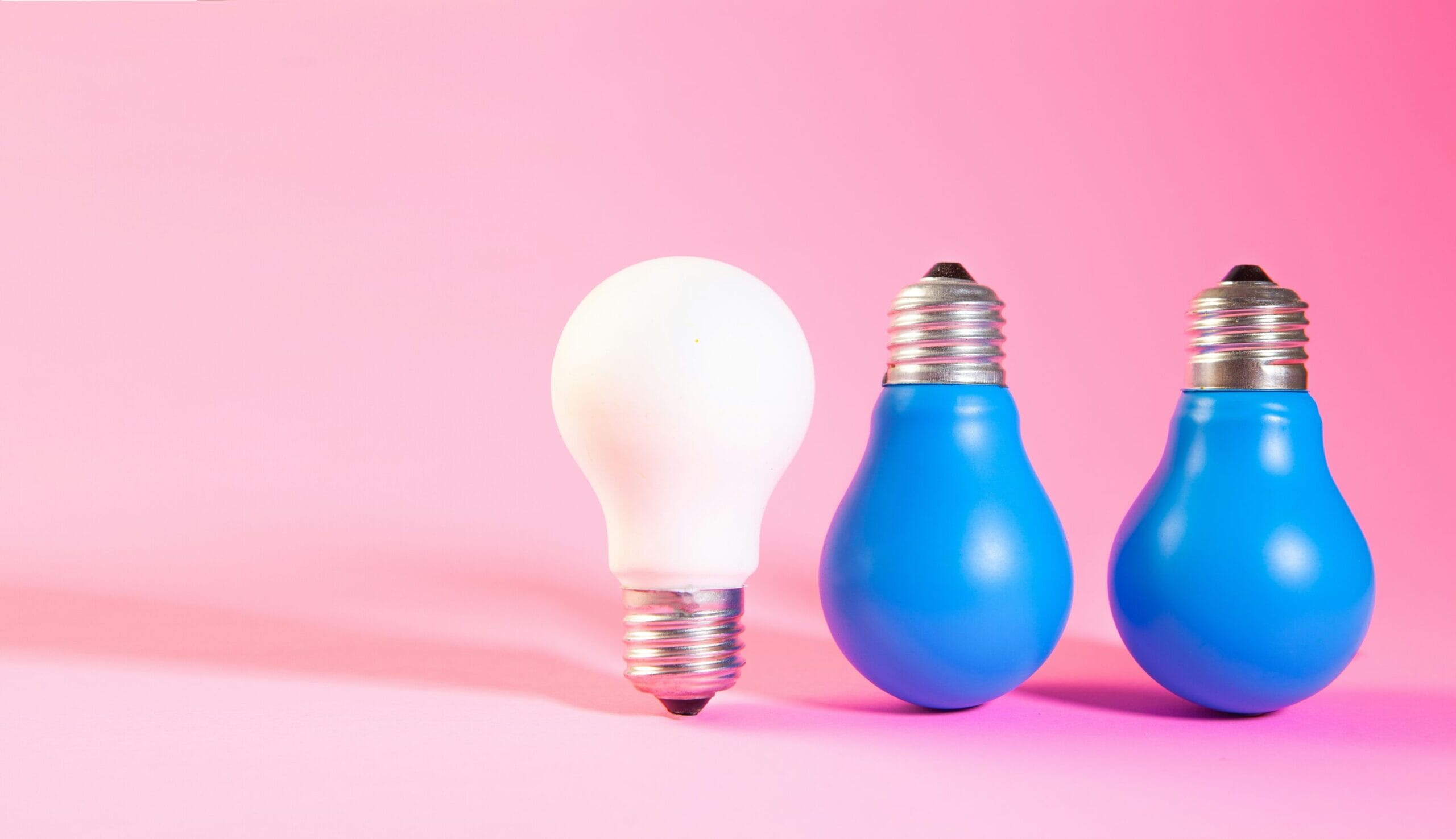 one white lightbulb and two blue lightbulbs on a pink background